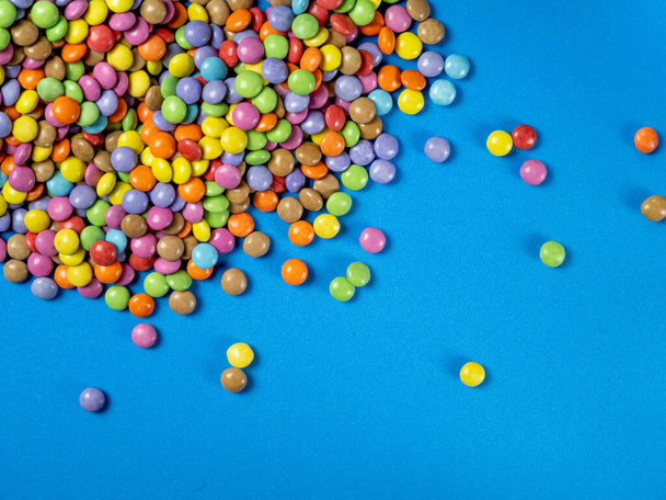 multicolored chocolat candy from left corner towards middle on blue background, copy space, close up - Photo, Image