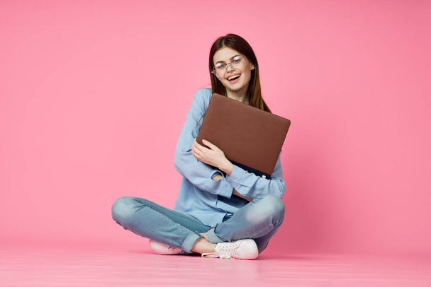 cheerful woman with laptop sitting on the floor on a pink background - Photo, image