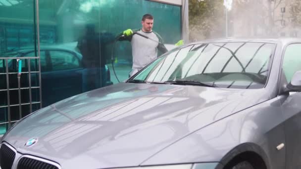 Egy fiatalember mossa a kocsiját víz nyomása alatt egy autómosóban.  - Felvétel, videó