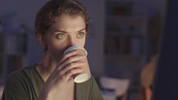 Середній крупний план вдумливої молодої жінки-програмістки, яка серйозно дивиться на екран комп'ютера і сіє каву з паперової чашки, залишаючись в офісі вночі
 - Кадри, відео