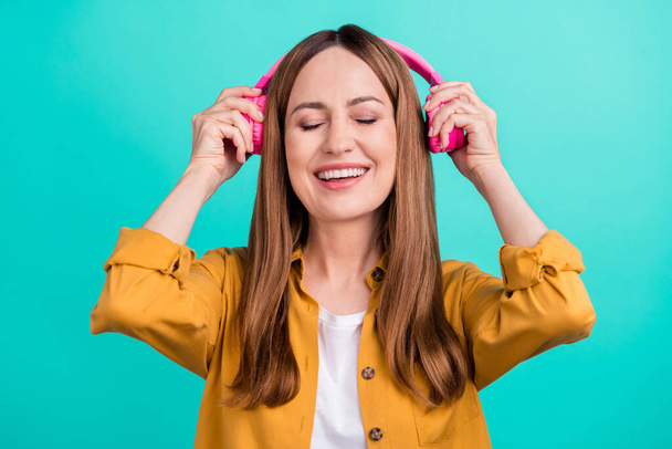 Photo of funny dreamy mature lady wear yellow shirt enjoying music headphones smiling isolated turquoise color background - Photo, Image