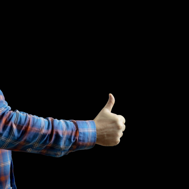 A mans hand in a checkered sleeve shows a thumb up on a black background. Gesture cool - Photo, Image