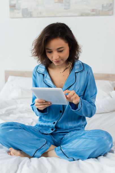 young woman in blue pajamas using digital tablet at home  - Foto, imagen