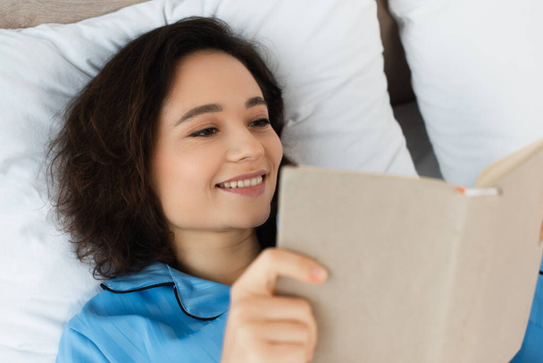 high angle view of cheerful young  woman reading book in bed - Foto, Bild