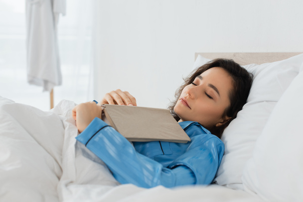young woman in blue pajamas sleeping with book in bed - Photo, Image