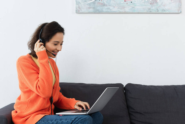 alegre joven mujer en auriculares usando el ordenador portátil en casa - Foto, imagen