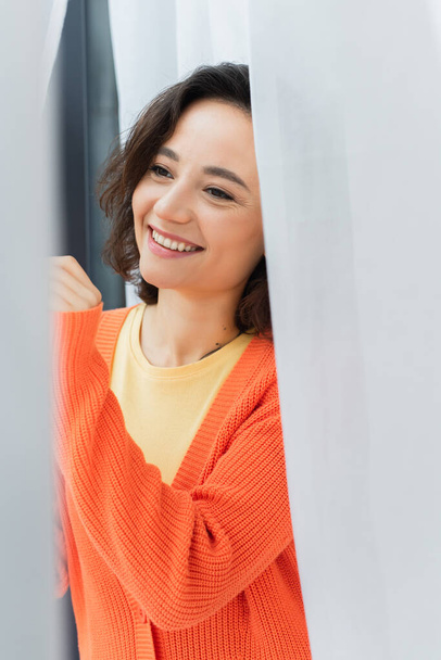 portrait of joyful young woman smiling near white curtain at home  - Φωτογραφία, εικόνα