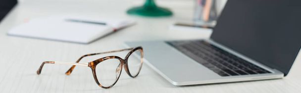 glasses near blurred laptop with blank screen on desk, banner - Zdjęcie, obraz