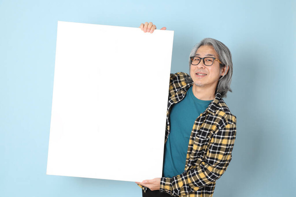 The senior Asian man with yellow plaid shirt standing on the blue background. - Photo, Image