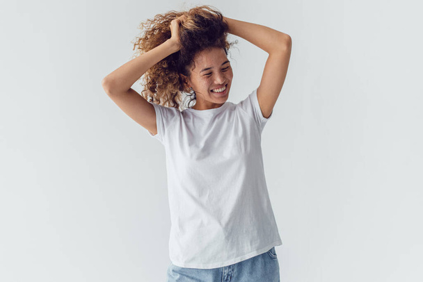 Smiling woman with lush curly hair in white blank t-shirt on a white background. Mock-up. - Fotografie, Obrázek