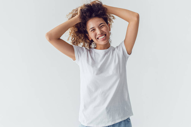 Smiling woman with lush curly hair in white blank t-shirt on a white background. Mock-up. - Fotoğraf, Görsel