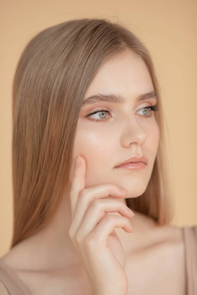 Retrato vertical de una hermosa joven rubia con la piel limpia, fondo beige. Cuidado de belleza cara concepto de moda
 - Foto, imagen