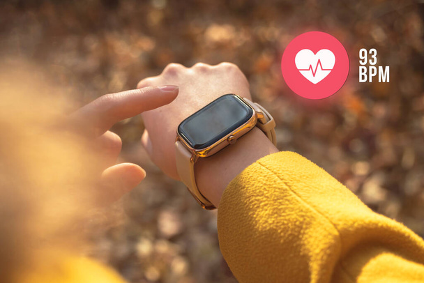 Chytré hodinky s ikonou srdeční frekvence, koncept zdravotní péče. Žena měření tepové frekvence venku - Fotografie, Obrázek