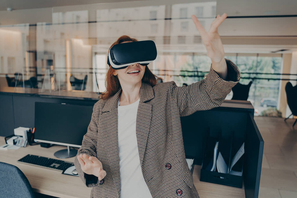 Trabalhadora de escritório usando headset de realidade virtual para visualizar e navegar arquivos no trabalho - Foto, Imagem