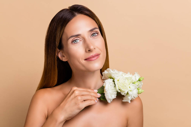 Photo of calm mature brunette lady with roses without clothes isolated over beige color background. - Valokuva, kuva