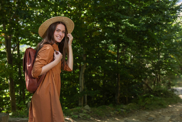 Happy woman with backpack and hat enjoying her walk in forest - Photo, Image