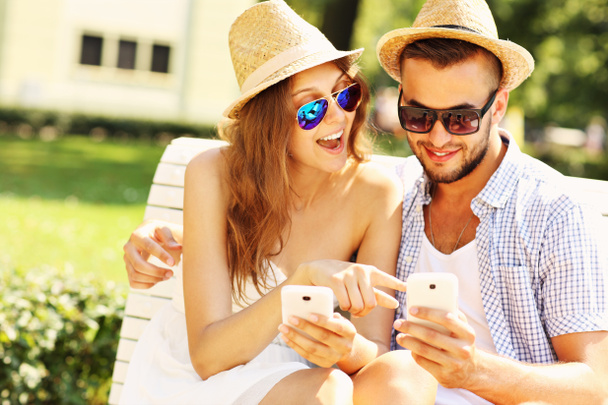 šťastný pár sedící na lavičce s chytrými telefony - Fotografie, Obrázek