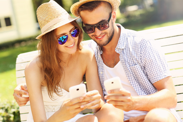 junges Paar sitzt mit Smartphones auf einer Bank - Foto, Bild
