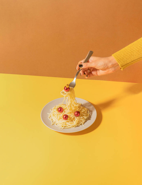 Creative retro scene with spaghetti plate and woman hand holding fork and red Christmas bauble against duo tone yellow and brown background. Vintage christmas dinner concept. - Foto, Imagem