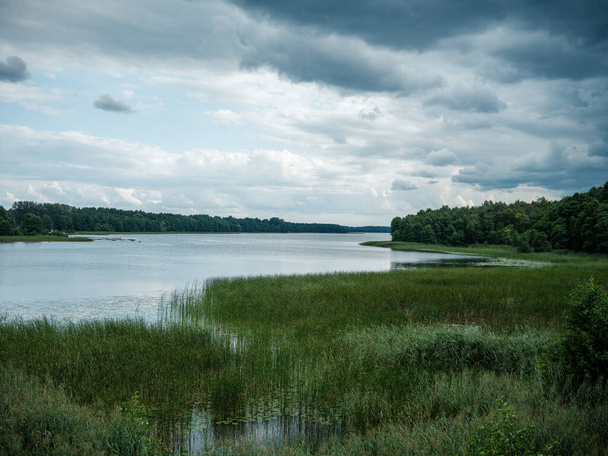 dramatyczne chmury nad błękitnym jeziorem latem otoczone ciemnymi drzewami - Zdjęcie, obraz