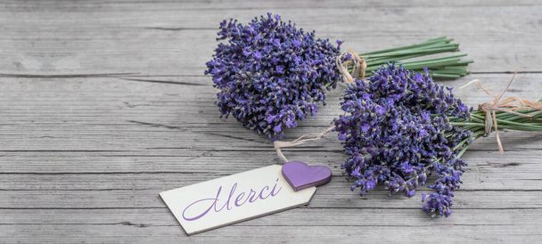 Primer plano de bouguet de violeta lavendula púrpura flores de lavanda hierbas con colgante de madera con la palabra: "Merci", en la vieja mesa de madera rústica, banner de fondo de madera panorama - Foto, imagen