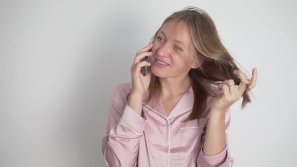 een gelukkig brunette vrouw in een roze huis shirt is praten op de telefoon - Video