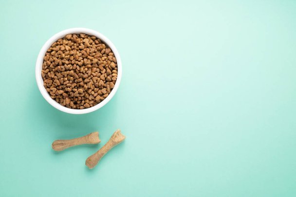 A full bowl of dry pet food and natural toothpicks. On a colored background, top view, copy space. - Foto, afbeelding