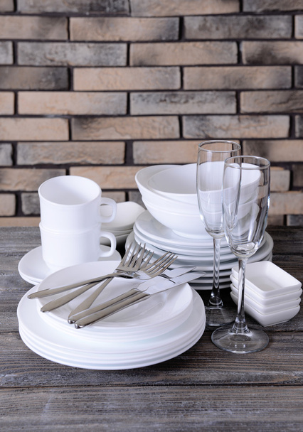 Set of white dishes on table on brick-wall background - Фото, зображення