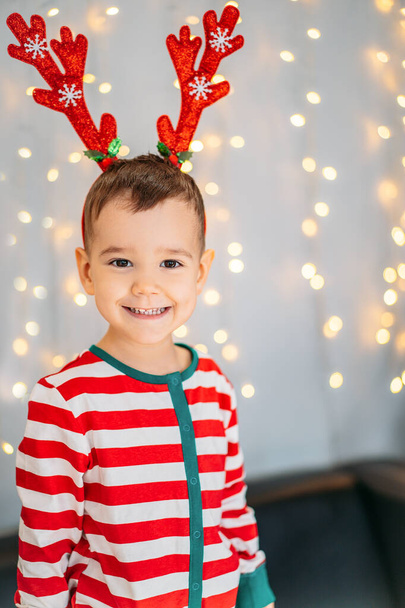 A lovely little baby is celebrating Christmas. New Year's holidays. Baby in Christmas pajamas on the background of Christmas lights. - Foto, imagen