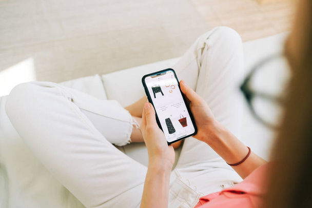 Young woman using online store app buying clothing. Woman at home lying on bed in living room using smartphone buys clothings in internet shop. - Valokuva, kuva