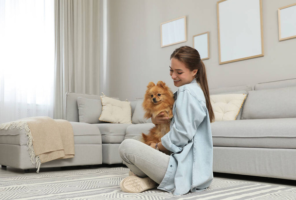 Happy young woman with cute dog in living room - 写真・画像