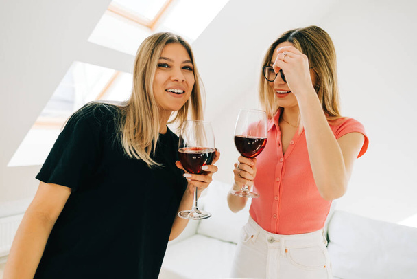Portrait of two young woman, friends heaving fun, drinking whine and celebrating success or spending their leisure time. - 写真・画像