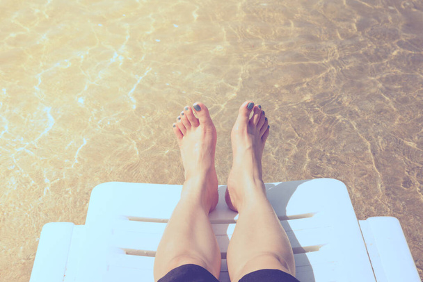 Tropikal plajda tatil. Plaj yatağında kadın bacakları. Temiz okyanus suyu arka planında. - Fotoğraf, Görsel