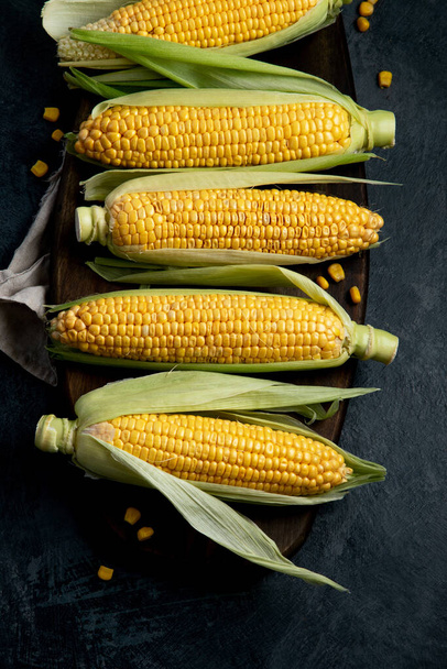 Сырая кукуруза или кукуруза на тёмном фоне. Концепция сбора урожая. Вид сверху, плоский, копировальное пространство - Фото, изображение