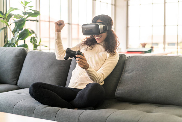 Mujer latina usando un auricular de realidad virtual en el sofá en casa - Foto, imagen