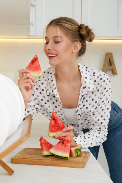 Beautiful teenage girl eating watermelon at countertop in kitchen - Foto, imagen