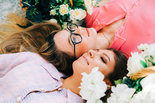 Portrait of two attractive caucasian woman lying on a floor with flowers. femininity concept - Foto, Bild