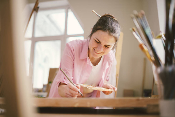 Art, creativity, hobby and creative occupation concept. Bringing creativity to life. Woman painting in art studio. Attractive female artist painting in workshop. Woman hobby, activity, profession. - Photo, Image