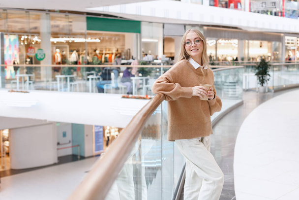a pretty woman in a sweater with a craft cup of coffee in mall - Foto, Imagem