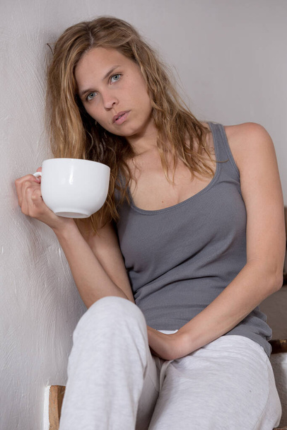 jong zielig uitziende vrouw in casual kleding met een kopje koffie zitten op de trap - Foto, afbeelding