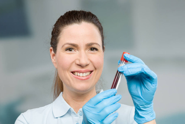 verpleegkundige of vrouwelijke wetenschapper met bloedmonster in een reageerbuis in een laboratorium - Foto, afbeelding