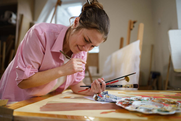 Female artist working in studio. Creative workspace, painting class, easel with canvas, art therapy. Inspiration, creativity, talent, craft concept. Artist studio interior. People, leisure and hobby. - Photo, Image