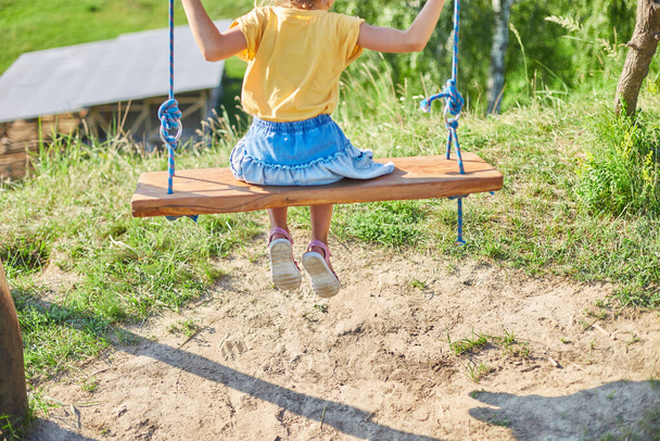 Similing little girl swinging on a large rustic wooden swing in the park, sunlight, summer freedom, beatuful view - Foto, afbeelding