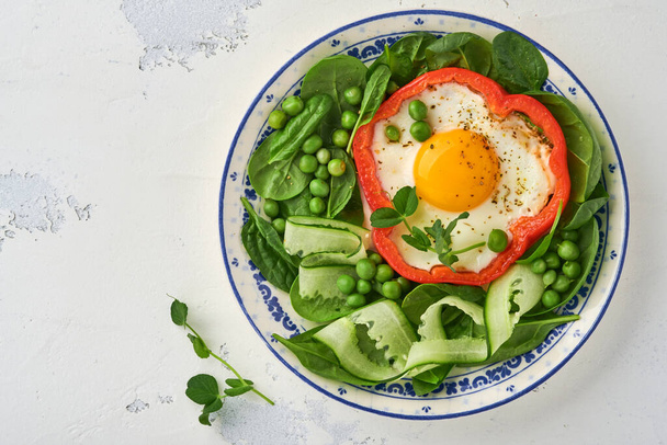 Red bell peppers stuffed with eggs, spinach leaves, green peas and microgreens on a breakfast plate on light grey table background. Top view. - Foto, Imagem