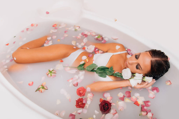 Ylellinen kylpylä nainen. elegantit silmät glamour tyttö silkki iho hauskaa makaa vesihauteessa rentouttava keskuudessa ruusun terälehtiä. Nainen ottaa wellness kylpy täynnä maitoa. - Valokuva, kuva