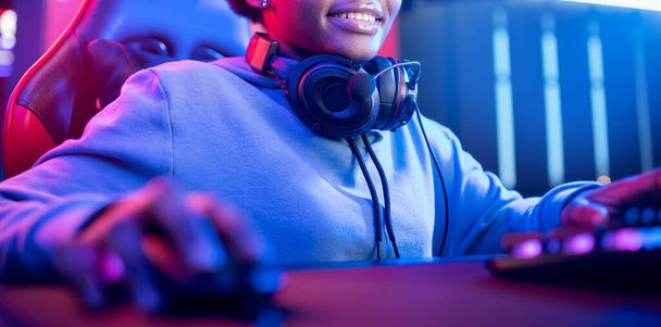 Estudio profesional de videojuegos cibernéticos afroamericano con sillón para computadora personal, teclado para flujo en fondo borroso de color neón, banner - Foto, imagen
