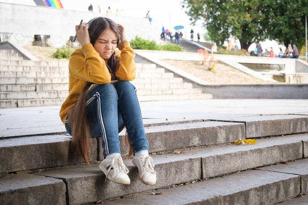 Una adolescente triste se sienta en las escaleras y se cubre la cabeza con las manos - Foto, Imagen