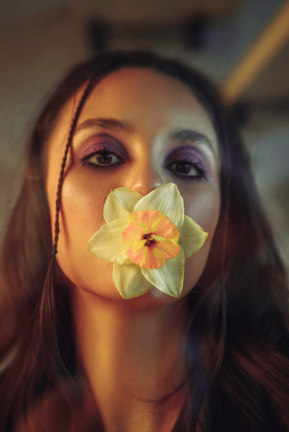 Jovem mulher atrás de uma parede de vidro com uma flor na boca. Retrato criativo. - Foto, Imagem