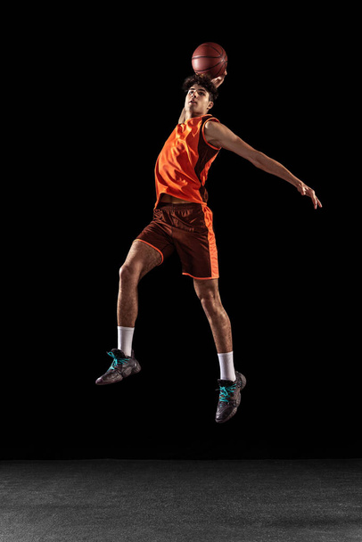 Ganzes Porträt des Basketballtrainings isoliert auf dunklem Studiohintergrund. Großer muskulöser Athlet springt mit Ball. - Foto, Bild