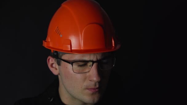 een man met een bril en een helm onderzoekt documenten op een donkere achtergrond - Video